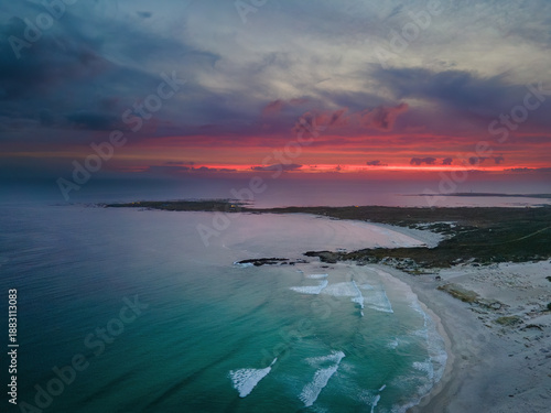 Aerial view of the tranquil turquoise ocean gently meeting the sandy shore under a fiery sunset sky, Betty's Bay, Western Cape, South Africa.