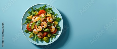 Overhead shot of a shrimp salad featuring spring vegetables such as arugula, tomato, avocado, and lemon dressing, served on a blue table with space for copy © The 2R Artificiality