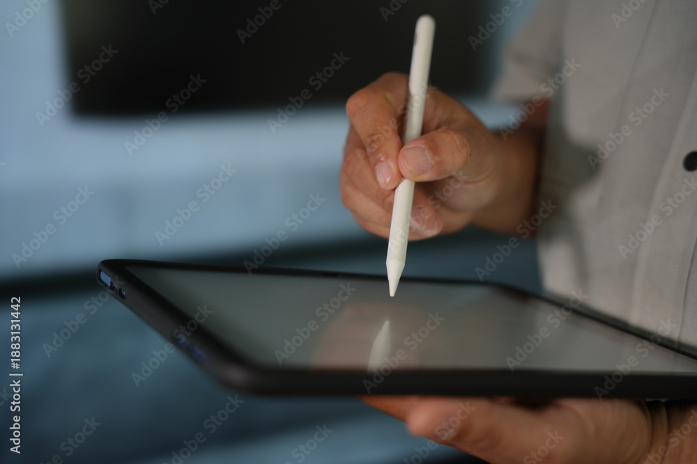Obraz premium A focused person uses a white digital stylus on a sleek tablet screen modern technology, creative design, and digital productivity within a clean, minimalist and contemporary workspace.