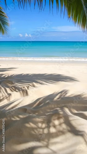 Idyllic tropical beach scene featuring turquoise ocean, blue sky, palm fronds, and patterns of shade cast on pristine golden sand.
