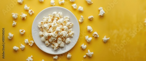Fresh popcorn on a white plate with a yellow background, close-up and selective focus, top view © AkuAku