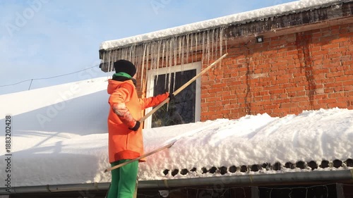Slow motion camera shot of Caucasian woman knocking down the icicles from the gutter. Female working outside during cold winter. Snowstorm.