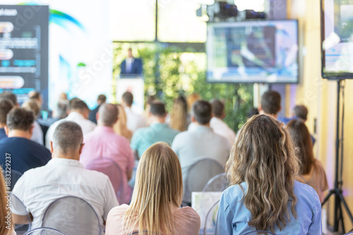Business conference audience attending keynote presentation in modern seminar hall, corporate event training with speaker on stage and screen