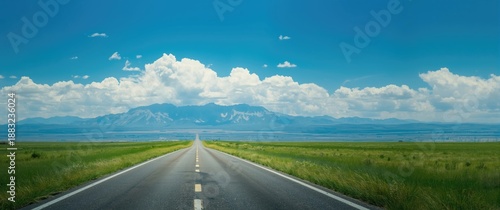 Deserted asphalt road surrounded by green grassland and mountain scenery under a blue sky