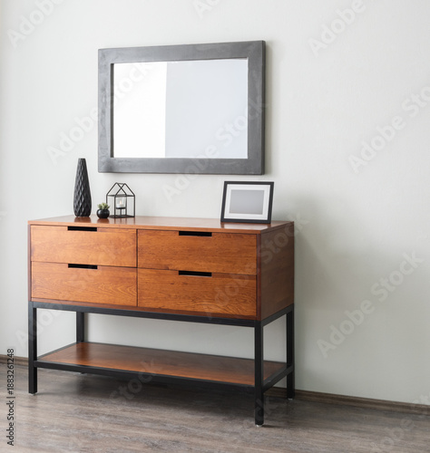 Photos Vintage Wooden Double-Drawer Nightstand in a Bright Modern Living Room, Adorned with Decorative Ornaments and a Picture Frame, Accompanied by a Wall Mirror Hanging on a White Wall, Wooden Floor