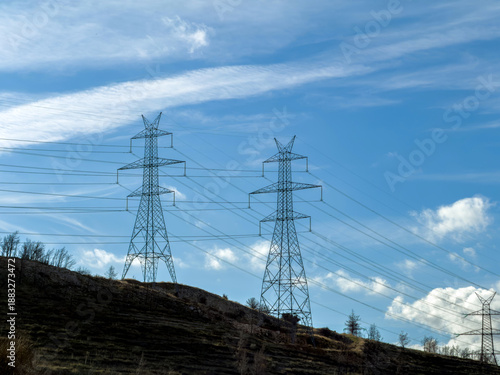 High voltage power pylon under cloudy sky in Athens, Greece. Crossing transmission lines above bare winter trees