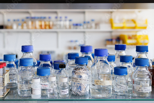 Transparent bottles with blue caps containing different chemical liquids on a shelve in a lab