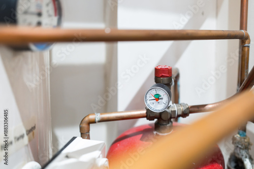 Shallow focus of a typical PSI water pressure gauge seen within a central heating system closet of a typical home. On the left is a hot water storage tank and is pressure and temp gauge.