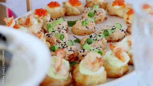 Variety of gourmet canapes arranged on a platter, featuring shrimp, salmon, cucumber, red caviar, and black sesame seeds, presented during a catered event
