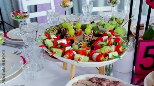 Vibrant vegetable skewers, sushi rolls, cheese cubes artfully arranged on white wooden legged platter, adorning elegant party spread