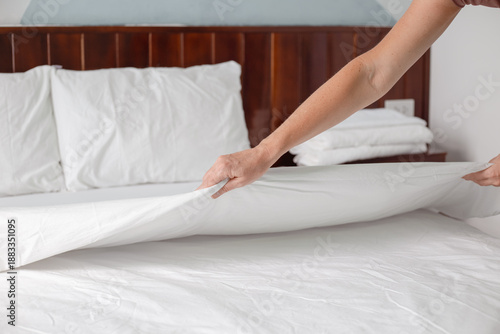 Foto A womans hands tuck a crisp white blanket into a freshly made bed in a bright bedroom