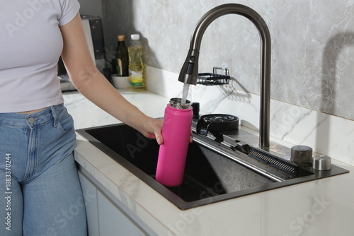 Konstfotografi kitchen setting showing a vibrant pink insulated water bottle being filled with water