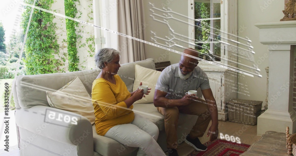 Fototapeta premium Sipping couple wearing gray polo and mustard top, holding white mugs in living-room by glass doors