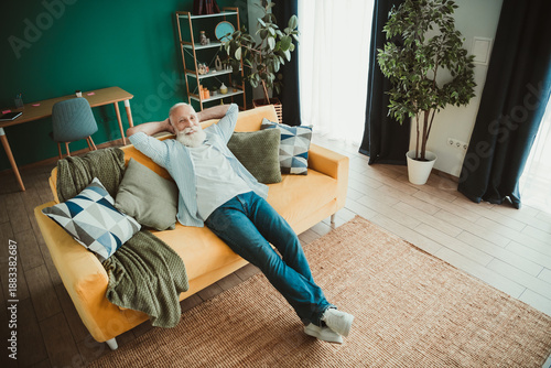 Bild auf Leinwand Relaxing senior man rests on a bright yellow sofa in a cozy living room at home