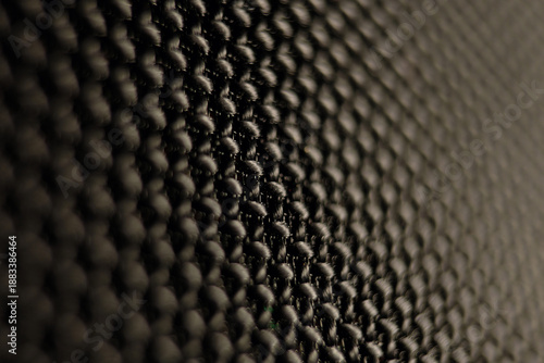 Macro close-up of a black woven mesh fabric texture with a rhythmic grid pattern. The interlaced threads create a dark, abstract background suitable for technology or acoustic concepts.