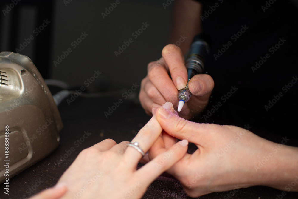 Obraz premium A nail technician removes gel polish from a clients nails using an electric nail drill