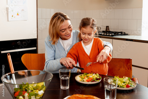 Mother teaching daughter healthy eating habits preparing salad for family dinner