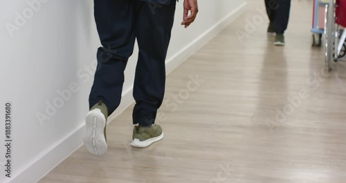 Doctor at hospital with stethoscope tapping tablet reviewing notes while passing nurse in scrubs