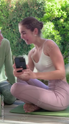 Vertical video: Leaning woman in white crop top and pink tights showing camera print to pal on deck