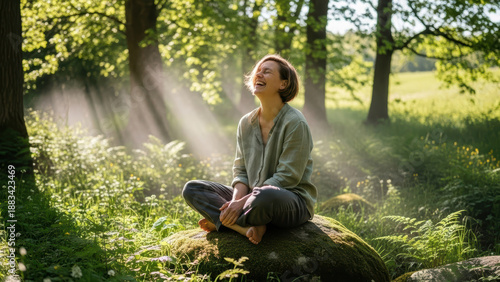 Woman sitting on rock in sunlit forest with arms raised, smiling