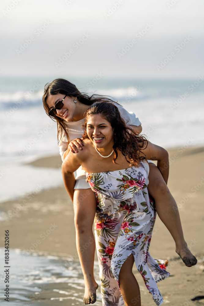 Fototapeta premium Young friends piggybacking on beach enjoying sunset