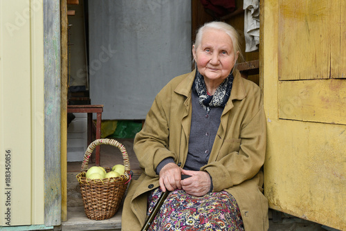A smiling elderly farmer woman sits on the porch of her old village house. A life of resilience.