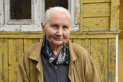 Portrait of a smiling elderly farmer woman with gray hair near her old village house