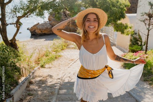 young attractive blond woman in summer style white dress and straw hat smiling having fun at the beach