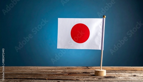 Small Japanese flag with red sun on white field mounted on wooden base, placed on rustic wood surface with blue gradient background. Free Download Small Japanese flag with red sun on white field mounted on wooden base, placed on rustic wood surface with blue gradient background. - GFXLoad