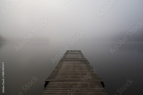 A foggy morning on the lake creates an atmosphere of peace and mysticism. A wooden pier, extending into the thick fog, emphasizes the depth and infinity of space. A minimalist Finnish autumn landscape