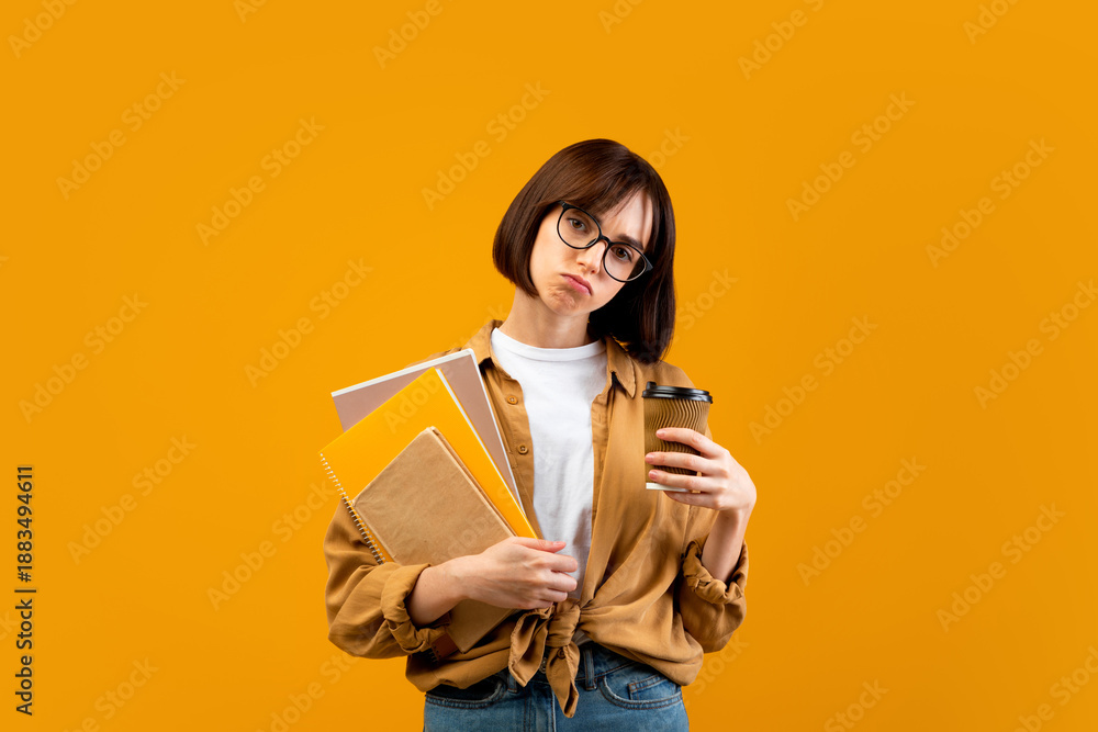 Obraz premium So tired. Exhausted female student with notebooks and takeaway coffee looking at camera on yellow studio background. Lady fatigue from preparing for college or university exams