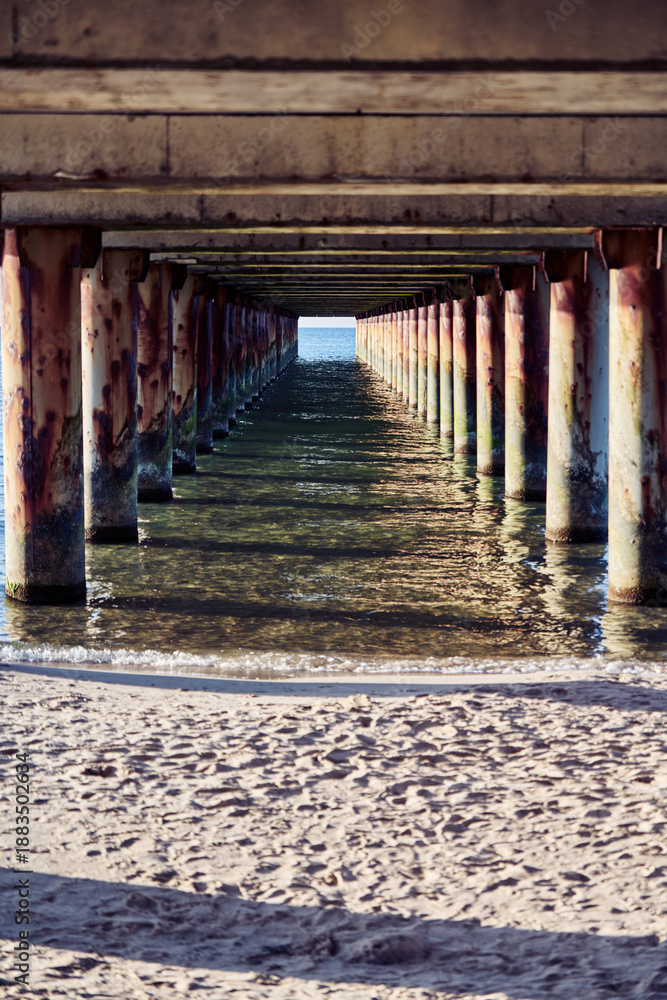 Fototapeta premium Rusted pier structure over Baltic Sea waters with Sandy Beach foreground