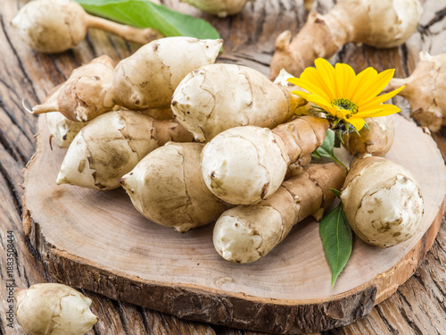 Obraz na płótnie Freshly harvested Jerusalem artichoke (sunchoke) tubers with a yellow flower and green leaves, arranged on a rustic wooden table