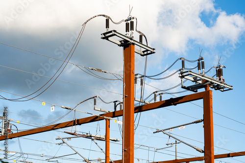 Train Power lines and equipment stand tall at a train track, showcasing the complex infrastructure of energy distribution during a sunny day. The clear sky provides a vibrant backdrop