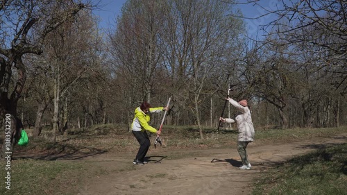 Instructor demonstrates Nordic walking pole technique to student in park. Spring warm up for caucasian women of different generations. Training for elderly people in sunny weather.