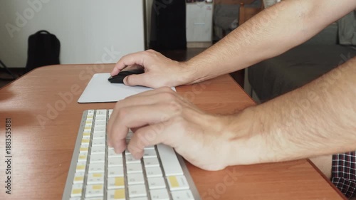 Keyboard and computer mouse on table in hands of caucasian man. Using computer and console, and controlling wireless mouse through scrolling and clicking. Wireless peripherals at home.