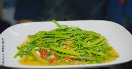 Freshly cooked stir-fried Asian water spinach (Pad Pak Boong) served steaming hot on a white plate, showcasing authentic Thai cuisine, vibrant flavors, and healthy vegetables.
