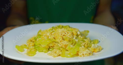 Flavorful Asian-inspired stir-fry with bitter melon and fluffy scrambled eggs, freshly presented on a clean white plate by a chef, highlighting healthy, homemade, and traditional Asian comfort food.