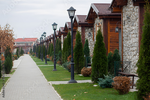 Row of wooden houses with stone walls and green trees along a pathway in a quiet neighborhood in autumn