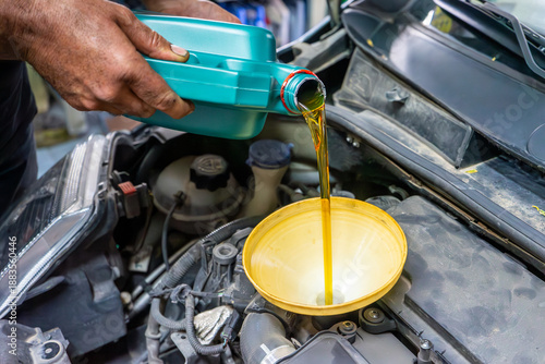 Close-up of a mechanic pouring engine oil into a car engine using a funnel, representing vehicle maintenance, oil change service, and automotive repair work.