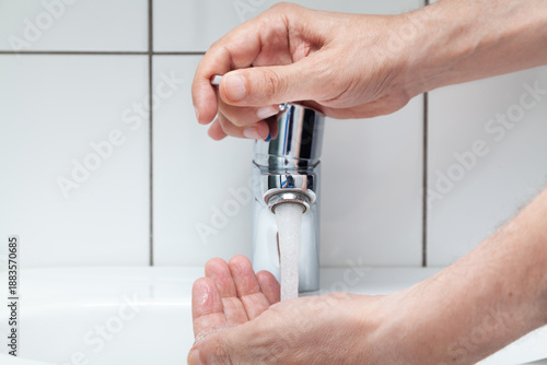 Quadro em tela Man washes his hands in a white sink close-up