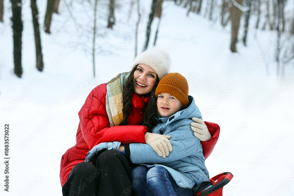 Obraz premium Happy mother and her son with sledge outdoors on winter day