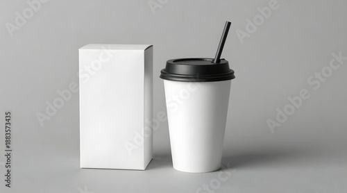 White disposable cup with black lid and straw next to small box on gray background