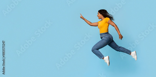 Fotografia Excited young black pretty lady jumping towards copy space, emotional african am