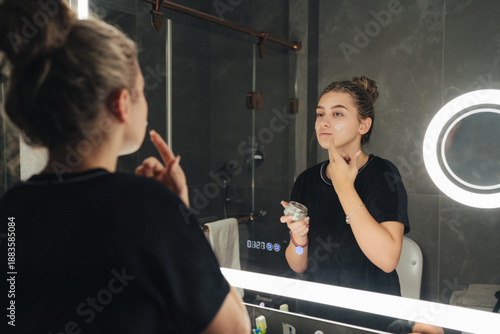 Modern Woman Focused On Skincare Routine Using Mirror And Soft Background Tones In Bathroom