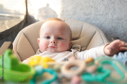 Child In Highchair Observes Camera Amidst Cheerful Toys And Engaging Sensory Objects In Cozy Setting