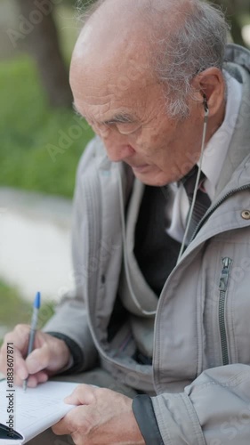 Elderly man writing on notebook sitting on bench