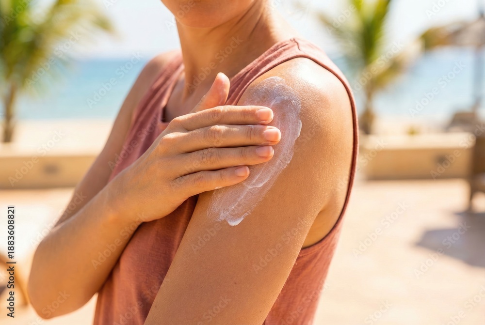 Fototapeta premium Applying sunscreen on shoulder at beach during sunny day near water with palm trees in background