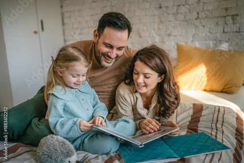 Foto Parents and daughter reading a book in bed enjoying family time