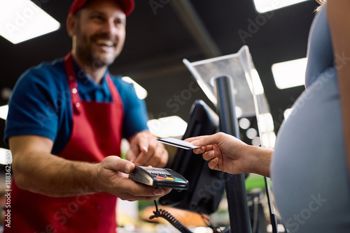 Close up of pregnant woman using credit car while paying bill at cash register.